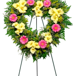 Heart-shaped floral wreath on a stand with pink daisies and pale yellow calla lilies