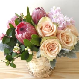 Bouquet of pale roses and pink protea in a birch bark container