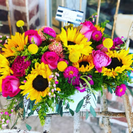 Bright bouquet with sunflowers, pink roses, and magenta flowers in a white container