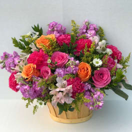 Mixed bouquet of pink, purple, and orange flowers in a wooden basket
