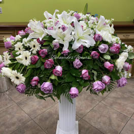 Large floral arrangement of white lilies, pink roses, and white daisies in a pedestal vase