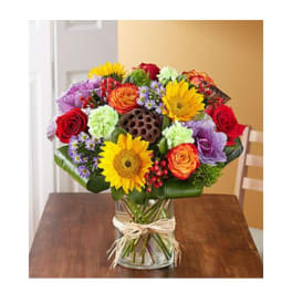 Mixed bouquet of roses, sunflowers, and daisies in a glass vase