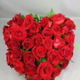 Heart-shaped bouquet of red roses with small green accents