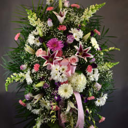 Large standing floral spray with lilies, daisies, roses, and pink ribbon