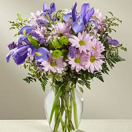 Purple irises and pink daisies in a clear glass vase