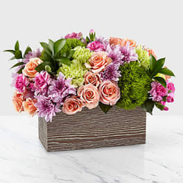 Mixed bouquet of pink, peach, and green flowers in a wooden box