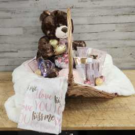 Gift basket with a teddy bear, chocolates, and beauty items on a white blanket