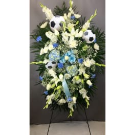 Standing floral spray with white flowers, blue accents, and soccer balls