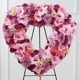 Heart-shaped floral wreath in pink and purple tones on a black stand