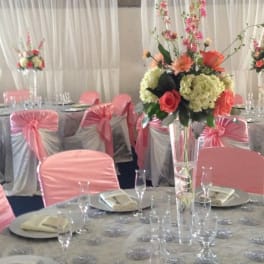 Tall floral centerpiece with pink and coral flowers in a clear vase at a decorated banquet table