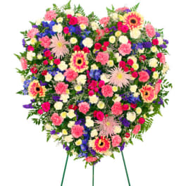 Heart-shaped standing spray of mixed pink, white, purple, and yellow flowers