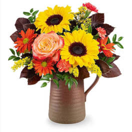Bouquet of sunflowers, roses, and orange daisies in a brown pitcher vase