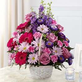 Mixed pink, purple, and white flowers in a white basket on a table