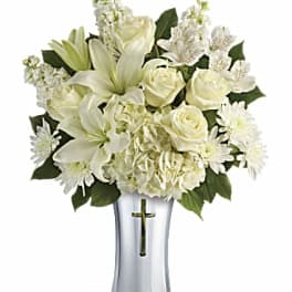 White lilies and roses arranged in a silver vase with a cross