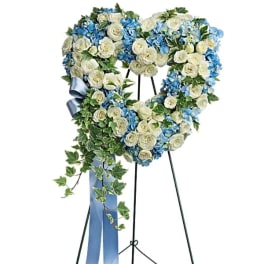 Heart-shaped floral wreath of white roses and blue flowers on a stand