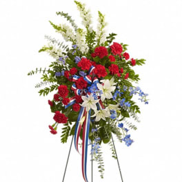 Standing floral spray with red carnations, white lilies, and blue accents on a tripod easel