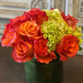 Orange and red roses with green hydrangeas in a glass vase