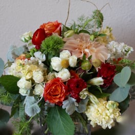 Mixed bouquet with orange, red, and white flowers in a glass vase