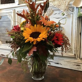 Autumn bouquet with a sunflower and orange lilies in a glass vase