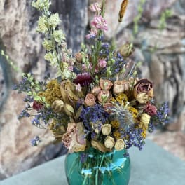 Dried flower bouquet in a teal glass vase