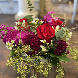 Red roses and magenta flowers arranged in a low vase