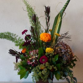 Tall mixed floral arrangement in a brown vase with orange and purple blooms