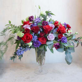 Mixed bouquet of red, purple, and pink roses in a clear glass vase