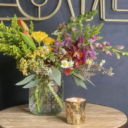 Mixed bouquet in a glass jar with a small gold candle holder beside it