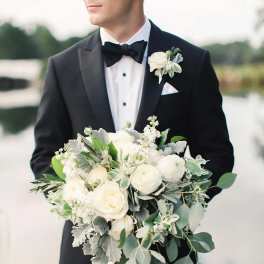 Man in tuxedo holding a white bridal bouquet with greenery