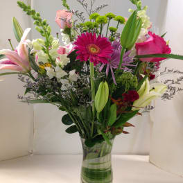 Mixed bouquet of lilies, roses, and daisies in a clear glass vase