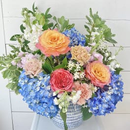 Colorful bouquet of roses, hydrangeas, and carnations in a white basket vase