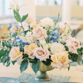 Pastel rose centerpiece in a pedestal vase with blue and white flowers