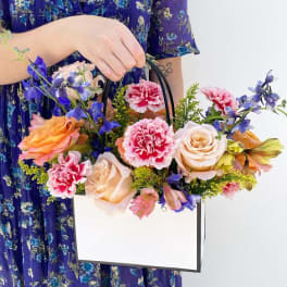 Handheld floral arrangement in a white box bag with roses and carnations