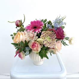 Mixed bouquet in a white vase with pink, peach, and blue flowers