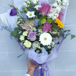 Handheld bouquet of mixed flowers in purple wrapping