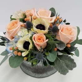 Peach roses and pale blooms arranged in a round metal container