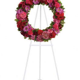 Circular floral wreath on a white easel with pink and red blooms