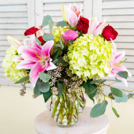 Bouquet of pink lilies, red roses, and green hydrangeas in a glass vase