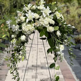White floral spray on a black stand with trailing greenery