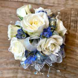 Small corsage of white roses and blue flowers with silver and blue ribbon accents