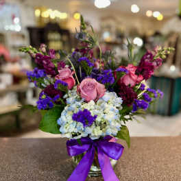Bouquet of pink roses, blue hydrangeas, and purple flowers in a glass vase