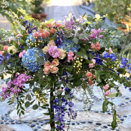 Large colorful floral arrangement with roses, hydrangeas, and hanging blooms