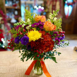 Colorful mixed bouquet in a glass vase with orange, yellow, purple, and red blooms