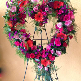 Heart-shaped floral wreath with pink and red flowers on a stand