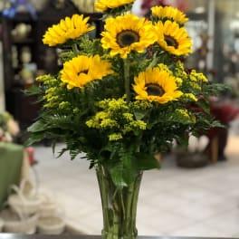 Tall clear vase of yellow sunflowers with small yellow filler flowers