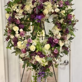 Heart-shaped floral wreath on a stand with cream, pink, and purple roses.