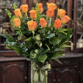 Tall arrangement of orange roses in a clear glass vase with a green ribbon bow