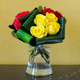 Bouquet of yellow, red, and pink roses in a clear glass vase