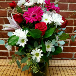 Bouquet of red roses, pink gerberas, and white daisies in a glass vase