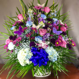 Colorful mixed flower arrangement in a white basket with a blue bow